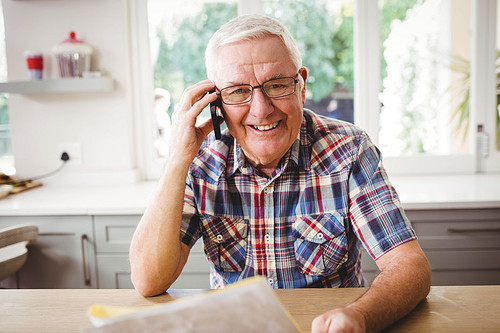 Senior man looking at a document while taking on phone at home