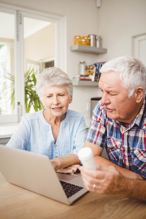 Senior couple holding a pill bottle and discussing while operating laptop