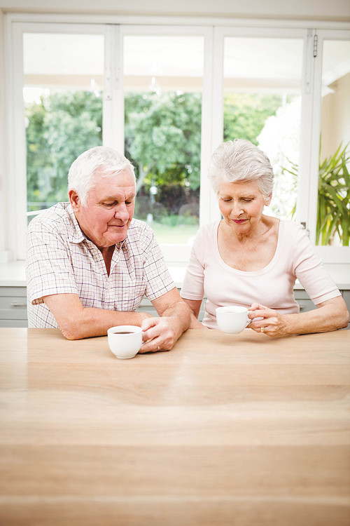 Senior couple talking to each other while having coffee in kitchen