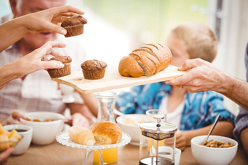 Close-up of hands passing cupcake and bread while having breakfast at home