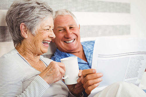 Senior couple laughing while reading newspaper in bedroom