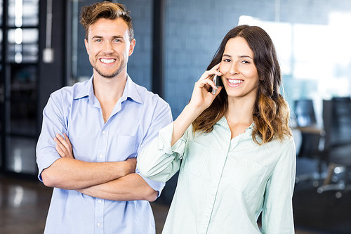 Confident executive talking on phone with female colleague standing beside in office