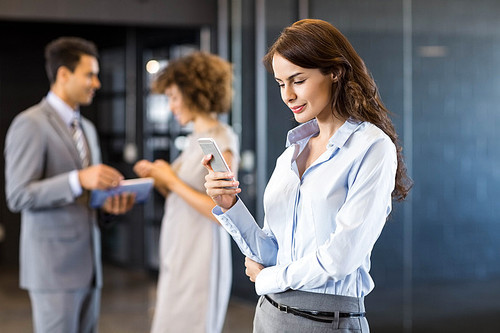 Businesswoman using mobile phone with a colleagues in background