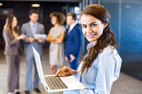 Confident businesswoman using laptop in office with her team in the background