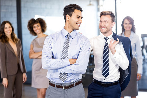 Smiling businessmen standing in front while businesswomen standing behind them in office