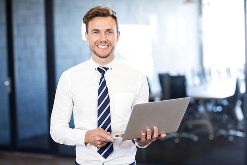 Portrait of businessman standing with a laptop in front conference room in office