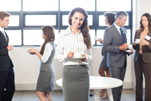 Successful businesswoman smiling at camera while her colleagues standing behind her in office