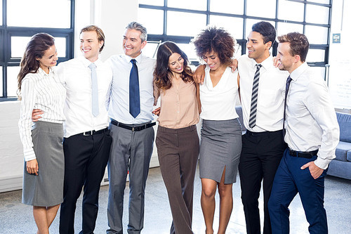 Businesspeople standing together with arms around each other in office