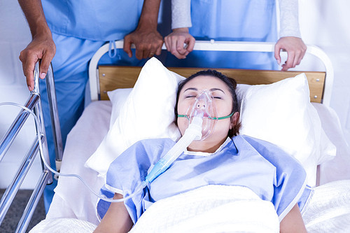 Patient with oxygen mask lying on bed and doctors standing near the bed