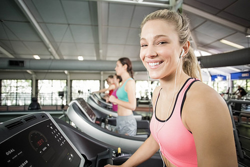 Fit woman running on the treadmill while listening music in crossfit
