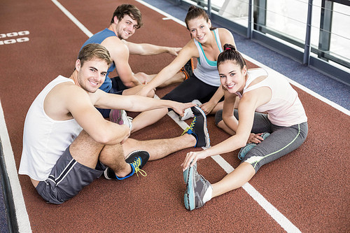 Four athletic women and men stretching on running track