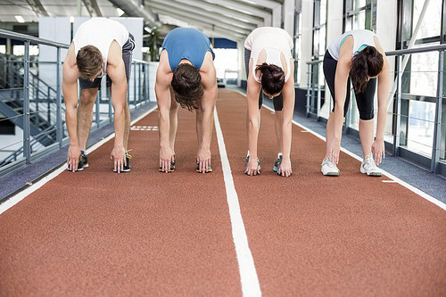 Four athletic women and men stretching on running track