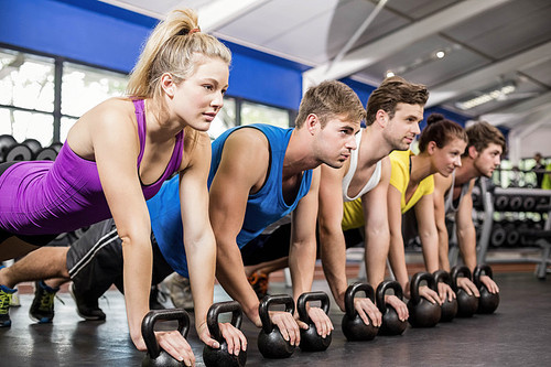 Fitness class in plank position with dumbbells in gym