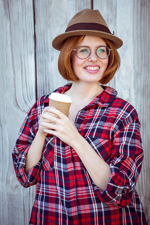 smiling hipster woman holding a coffee cup against a wooden background