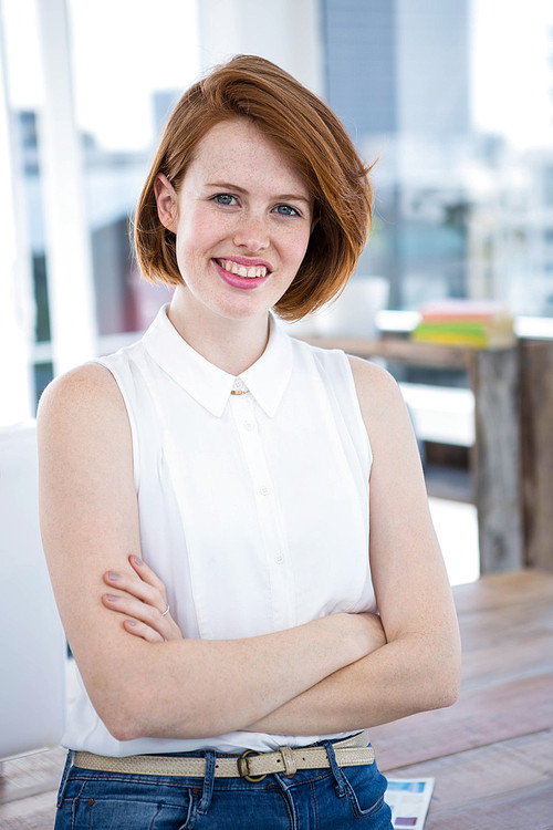 smiling hipster business woman standing in her office with her arms folded