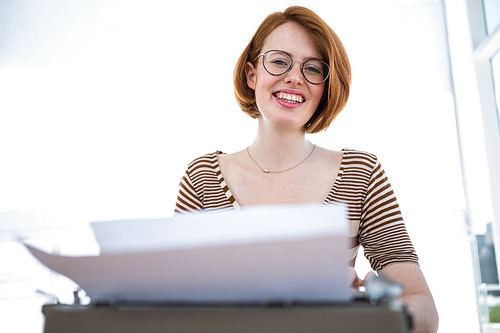 smiling hipster woman sitting at a desk, typing on her typewriter