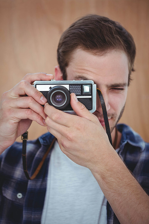 Handsome hipster taking picture with retro camera on a wooden background