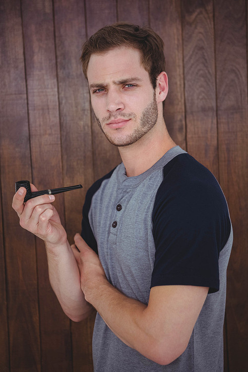 Handsome hipster smoking pipe on wooden background