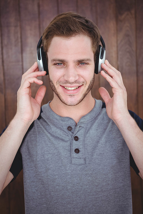 Handsome hipster listening to music with headphones on wooden background