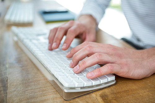 Masculine hands typing on keyboard in a bright office