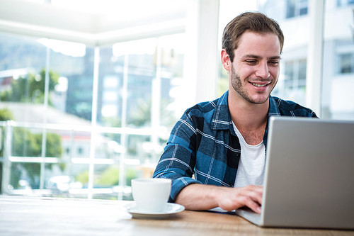 Handsome man working on laptop with cup of coffee in a bright office
