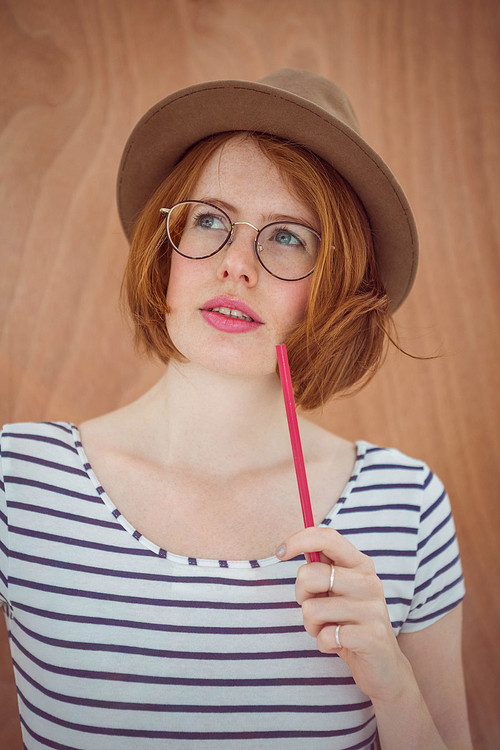 Thoughtful hipster holding pen on wooden background
