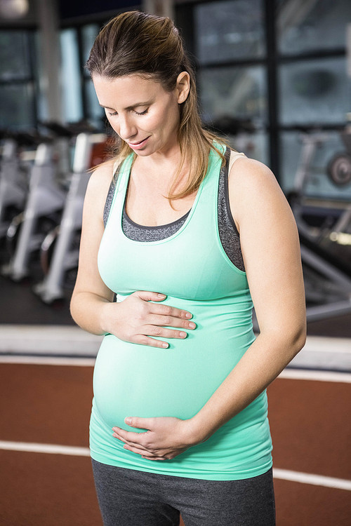 Pregnant blonde touching her belly at the gym