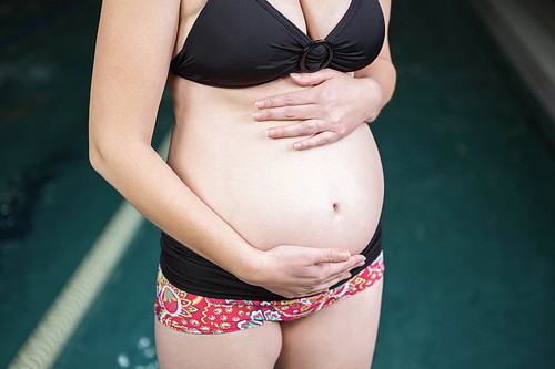 Mid section of pregnant woman standing next to the pool at the leisure center
