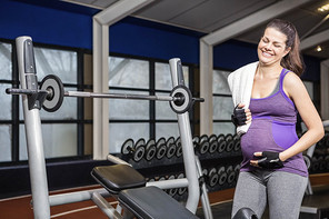 Smiling pregnant woman standing next to bench at the gym