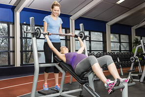 Smiling trainer helping pregnant woman lifting barbell at the gym