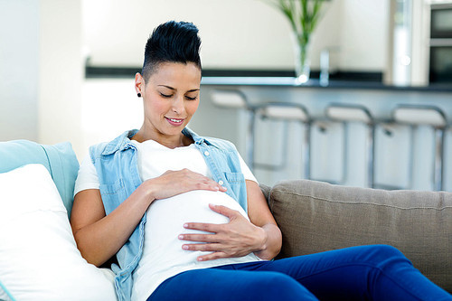 Pregnant woman touching her belly and relaxing on sofa in living room