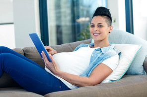 Portrait of pregnant woman using digital tablet while relaxing on sofa in living room