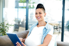 Portrait of pregnant woman using digital tablet while relaxing on sofa in living room
