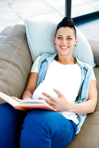 Portrait of pregnant woman reading a book while lying on sofa in living room