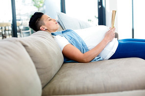 Pregnant woman reading a book while lying on sofa in living room