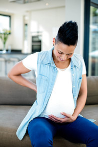 Pregnant woman with hand on stomach sitting on sofa in living room