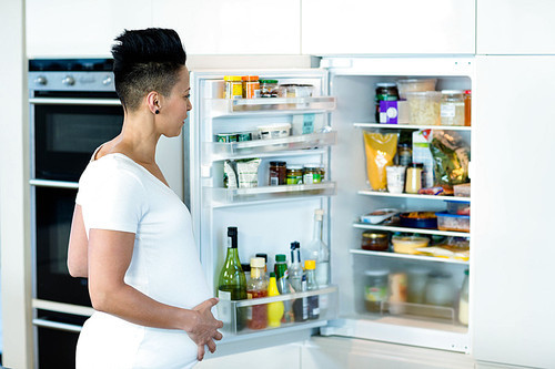 Pregnant woman looking in the fridge at home in the kitchen
