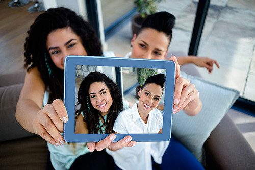 Lesbian couple sitting on sofa and taking a selfie with digital tablet