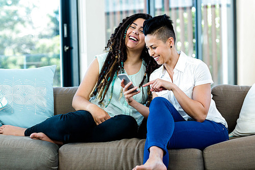 Lesbian couple looking at mobile phone and smiling in living room