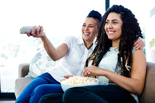 Lesbian couple sitting on sofa and watching television with a bowl of popcorn