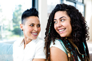 Happy lesbian couple sitting back to back in living room