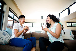 Lesbian couple smiling while having a cup of coffee in living room