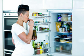 Pregnant woman standing near open refrigerator and eating pickles