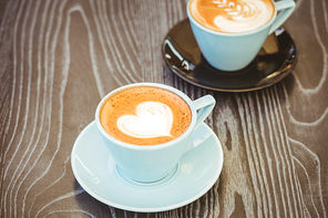 Cup of cappuccino with coffee art on wooden table at coffee shop