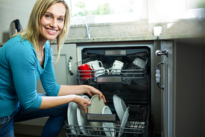 Pretty blonde woman emptying the dishwasher in the kitchen