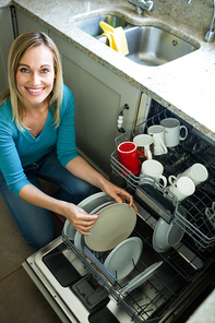 Pretty blonde woman emptying the dishwasher in the kitchen