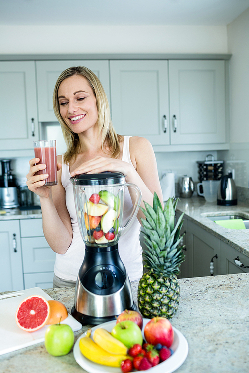 Pretty blonde woman holding her homemade smoothie in the kitchen