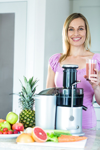 Blonde woman holding a smoothie glass in the kitchen at home