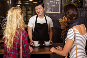 Smiling waiter serving a coffee to customers at the coffee shop
