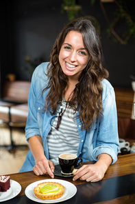 Smiling brunette drinking coffee and eating pastry at the coffee shop